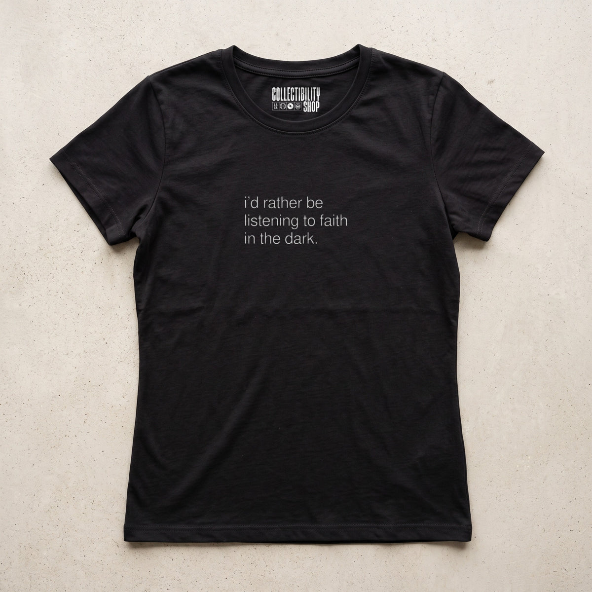 Black women's tee, flat lay, with small light grey lowercase type reading i'd rather be listening to faith in the dark. and the Collectibility Shop label inside the neck